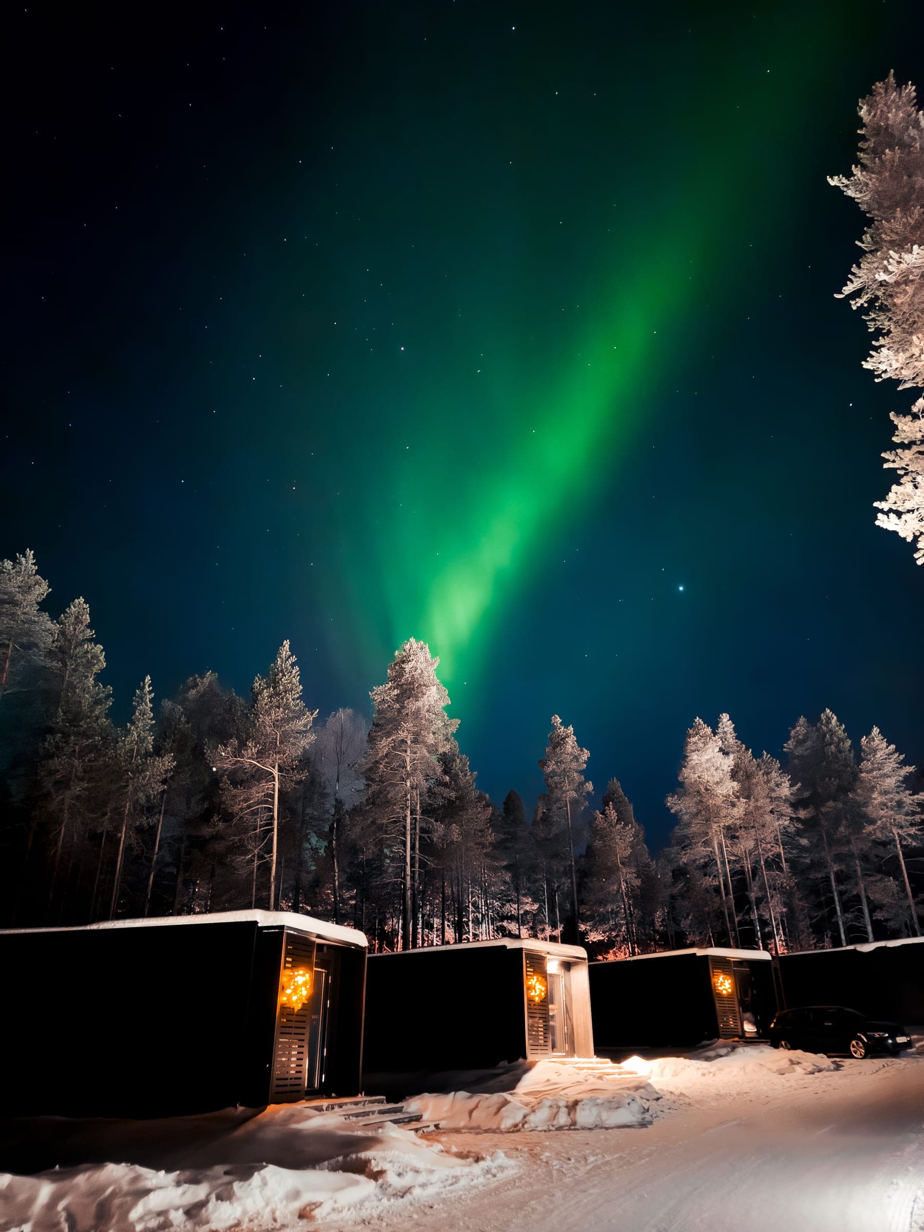Un arco de aurora verde sobre la fila de suites, con sus ventanas iluminadas con luz cálida